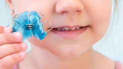 Niña sosteniendo una ortodoncia removible de color azul en clínica de odontopediatría
